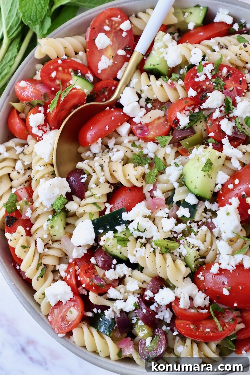 pasta salad with cucumber and tomatoes in a bowl with a spoon