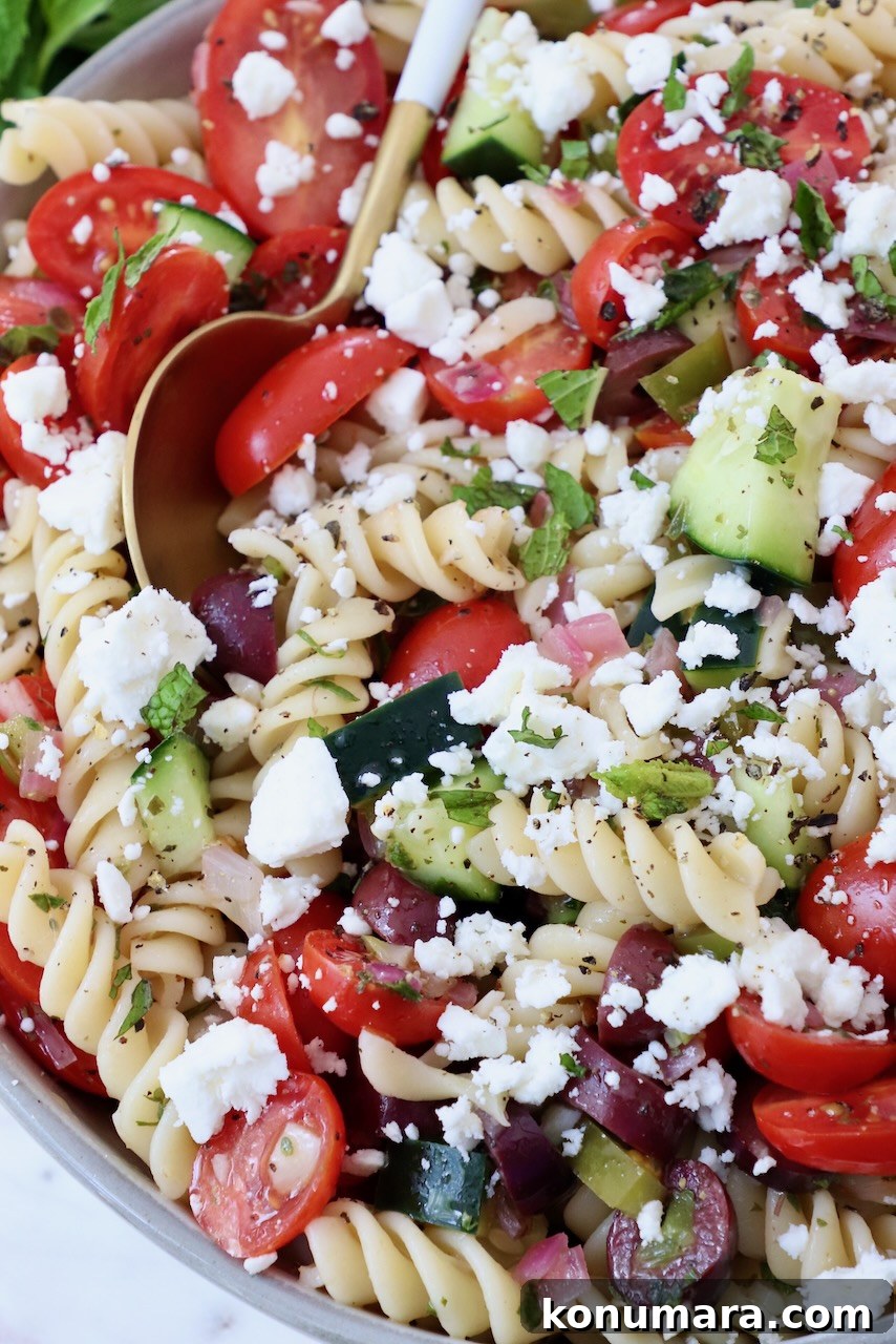 pasta salad topped with crumbled feta cheese in a bowl with a spoon