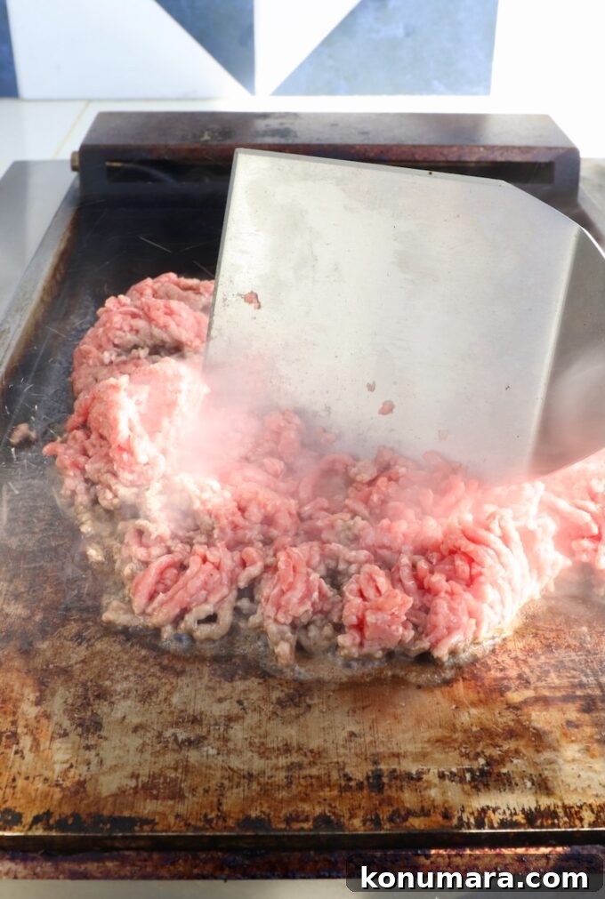 New York Bodega Chopped Cheese Sandwich Recipe 6 ground beef on a flat top griddle with a large metal spatula in the beef