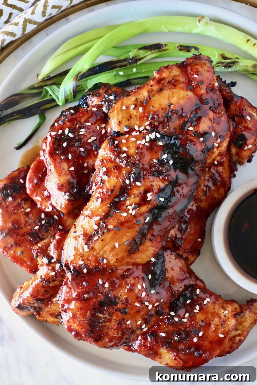 Korean BBQ Chicken with Gochujang Glaze 2 grilled chicken covered in bbq sauce stacked up on a plate with green onions on the side