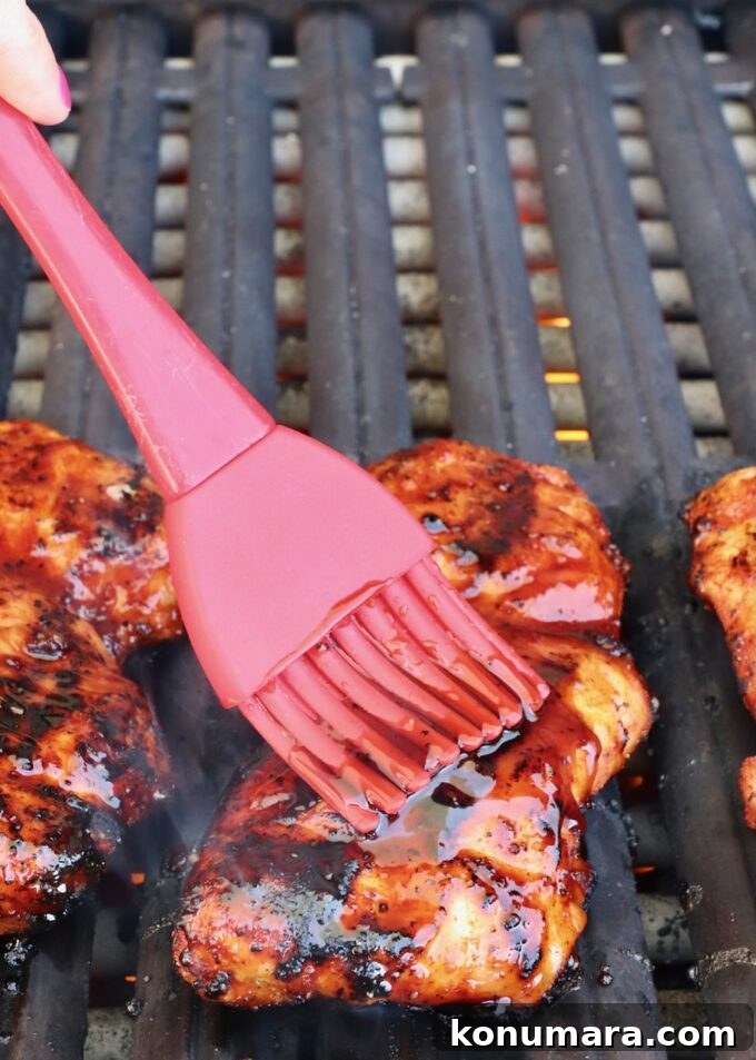 Korean BBQ Chicken with Gochujang Glaze 7 red brush with bbq sauce brushed on a grilled chicken thigh on a grill