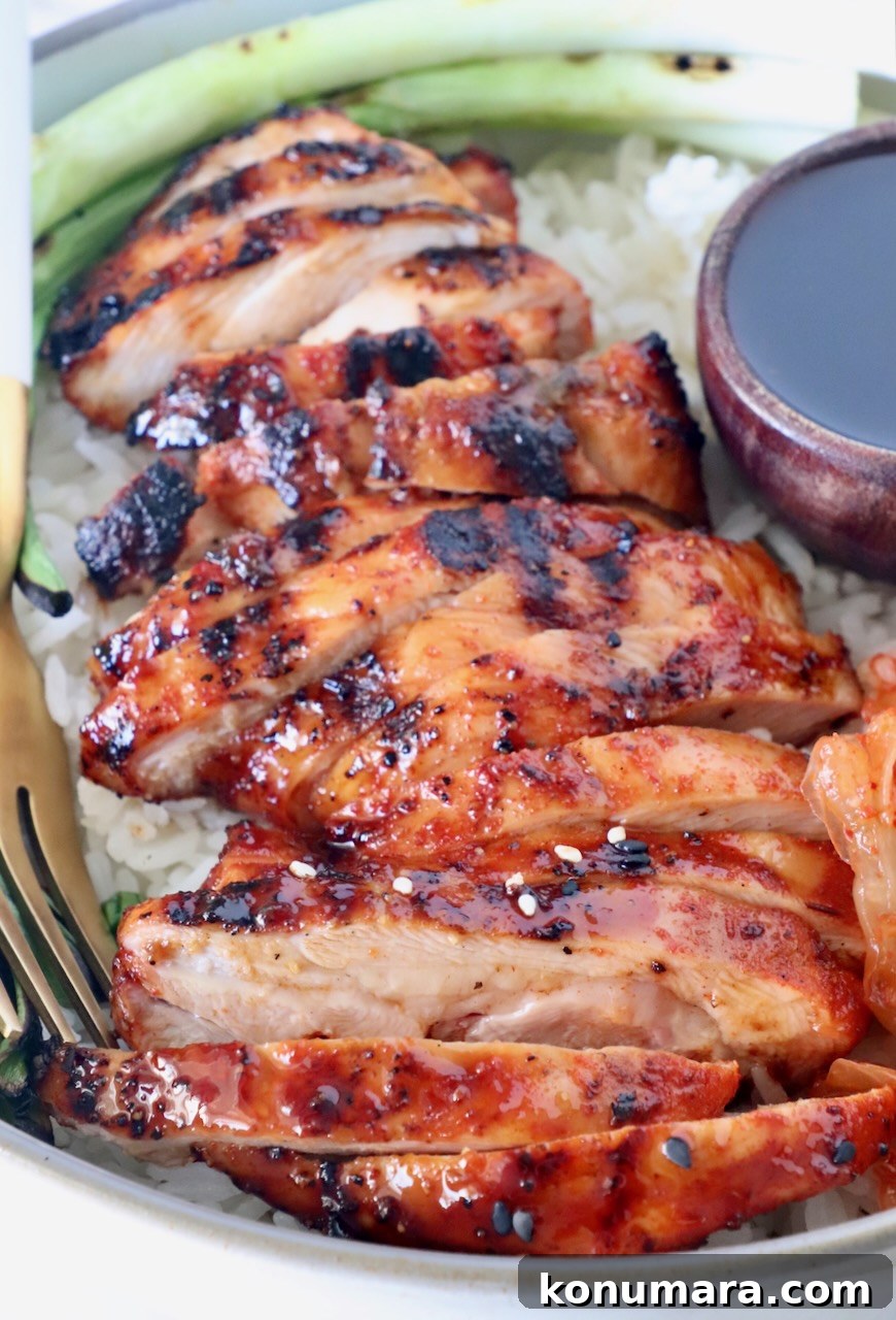 Korean BBQ Chicken with Gochujang Glaze 8 sliced grilled chicken thigh covered in bbq sauce over rice in a bowl with green onions and a small bowl of bbq sauce