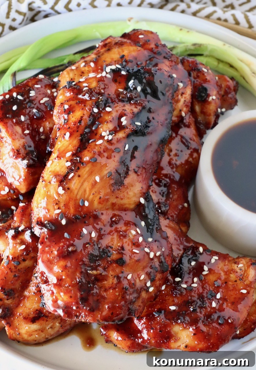 Korean BBQ Chicken with Gochujang Glaze 9 grilled chicken thighs stacked up on a plate glazed with bbq sauce, with green onions and Korean bbq sauce on the side of the plate