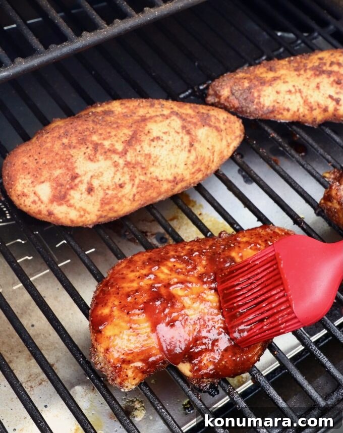 red brush with bbq sauce being brushed on a chicken breast on a smoker