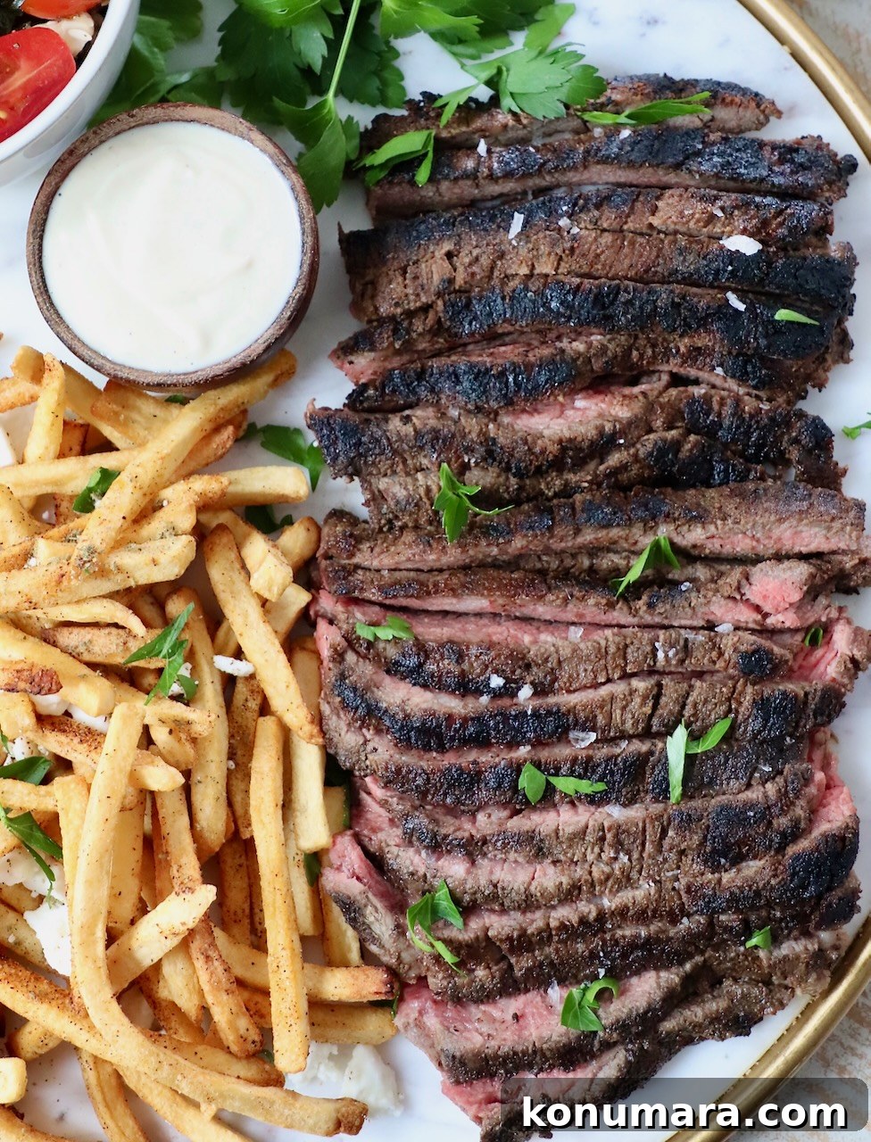 sliced steak on a platter with french fries and a small bowl of sauce