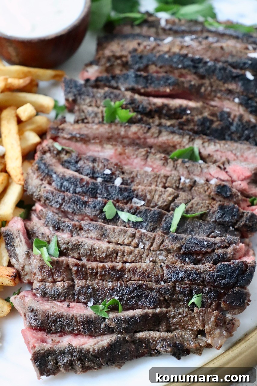sliced steak on a platter with french fries and a small bowl of sauce on the side