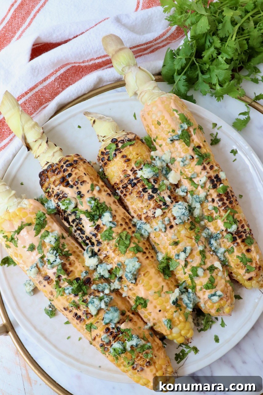 grilled corn on the cob on a plate topped with blue cheese crumbles and fresh cilantro