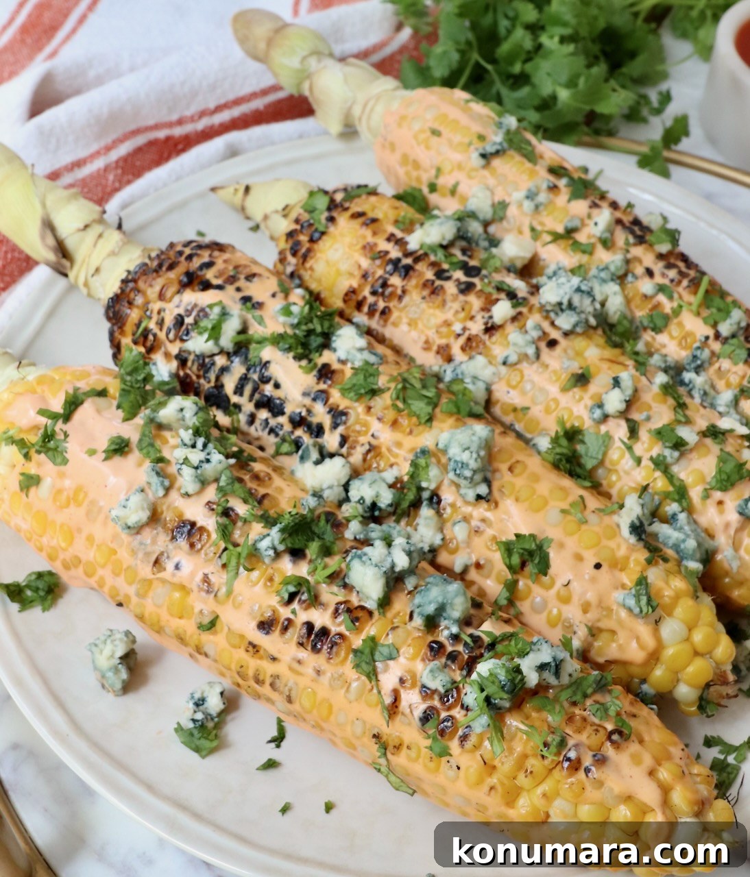 grilled corn on the cob on a plate, topped with blue cheese crumbles and chopped cilantro