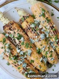 grilled corn on the cob on a plate topped with blue cheese crumbles and fresh chopped cilantro