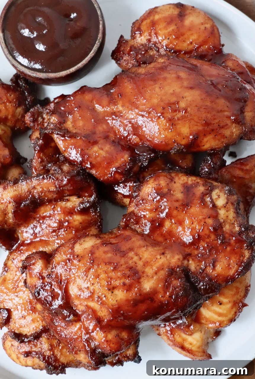 smoked chicken thighs glazed with bbq sauce stacked up on a plate with a small bowl of bbq sauce on the side