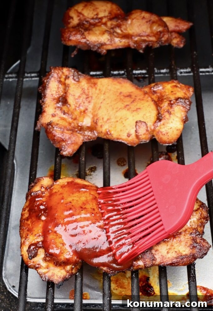 chicken thighs brushed with bbq sauce with a red brush on a smoker
