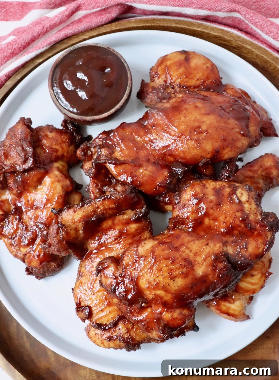 smoked chicken thighs stacked up on a plate with a small bowl of bbq sauce on the side