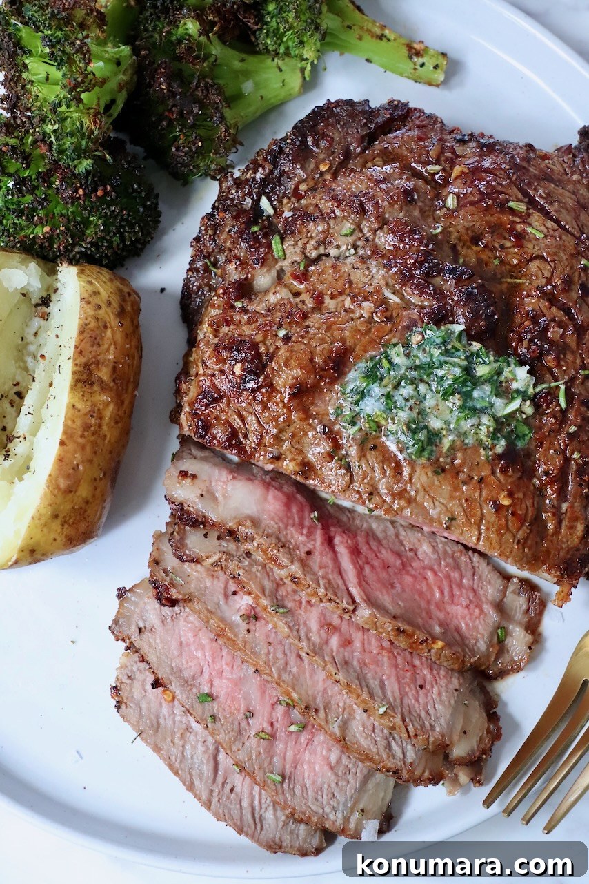 partially sliced ribeye steak on a plate with herb butter on top, cooked broccoli and a baked potato on the side