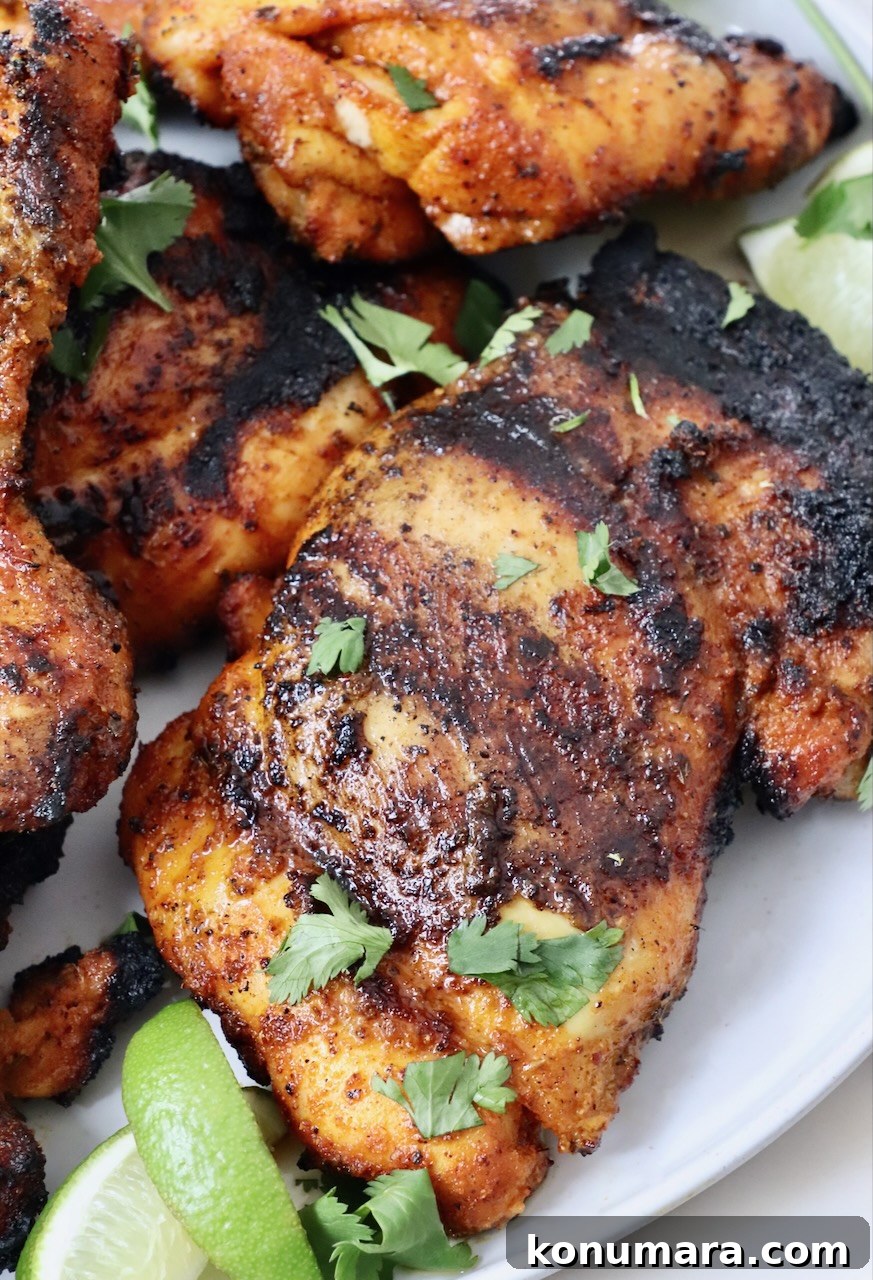 grilled chicken thighs stacked up on a plate with lime wedges on the side