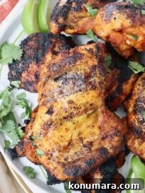 grilled chicken thighs stacked up on a plate with fresh cilantro and lime wedges