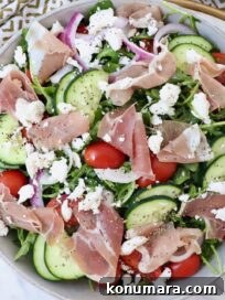 salad in a bowl with prosciutto, sliced cucumbers, feta cheese and tomatoes