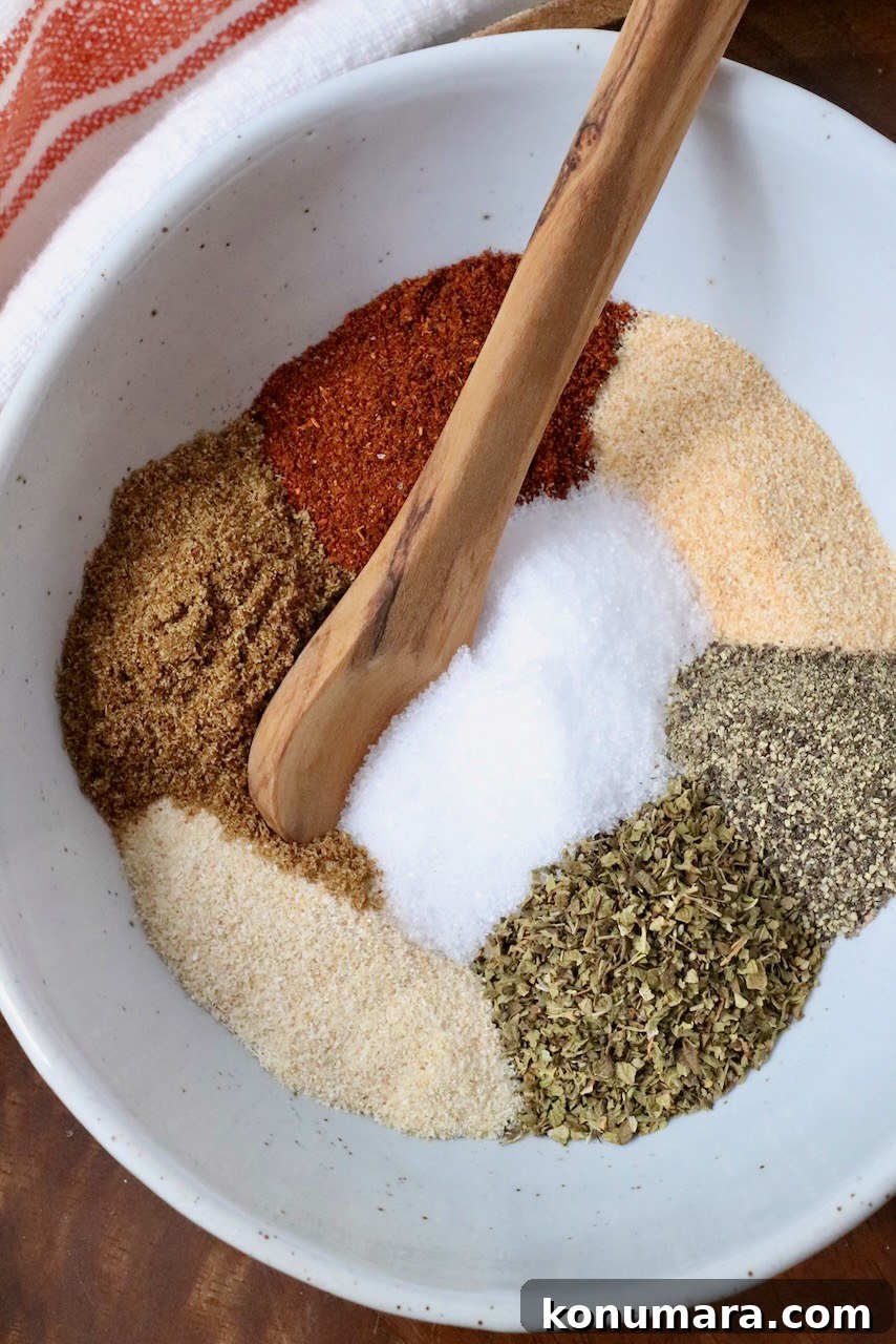 Authentic Carnitas Seasoning Recipe for Tender Pork 5 dried herbs and spices separated in a bowl with a wooden spoon