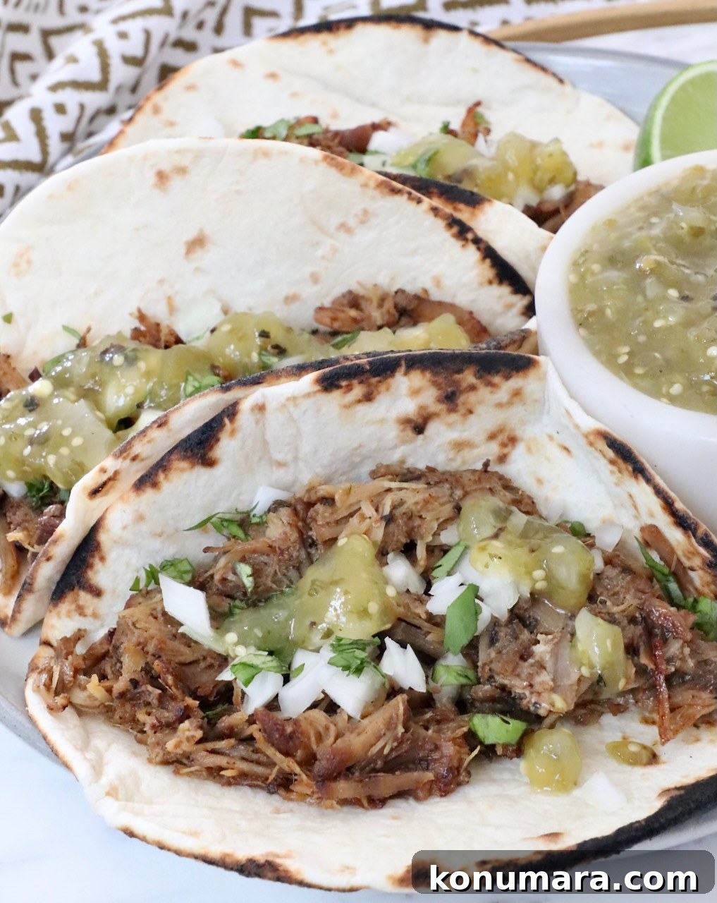 carnitas tacos on a plate with tomatillo salsa on the tacos and in a bowl on the side