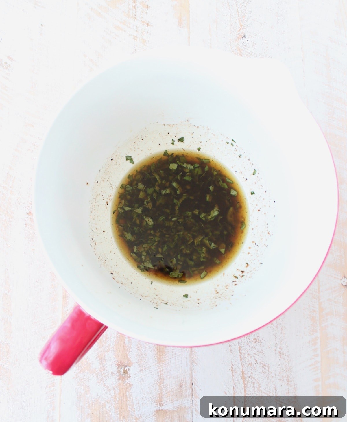 olive oil, basil, parsley, balsamic vinegar, lemon juice, salt and pepper in a white and red bowl.