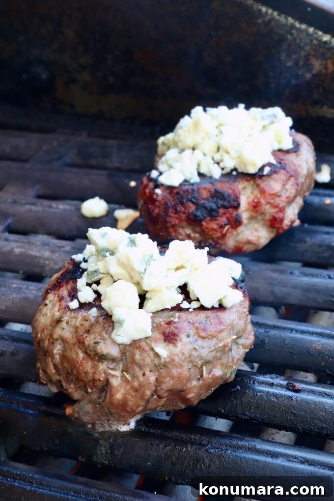 Grilled Mediterranean Lamb Burger with Mint Yogurt Sauce 7 cooked lamb burger patties on a grill topped with blue cheese crumbles