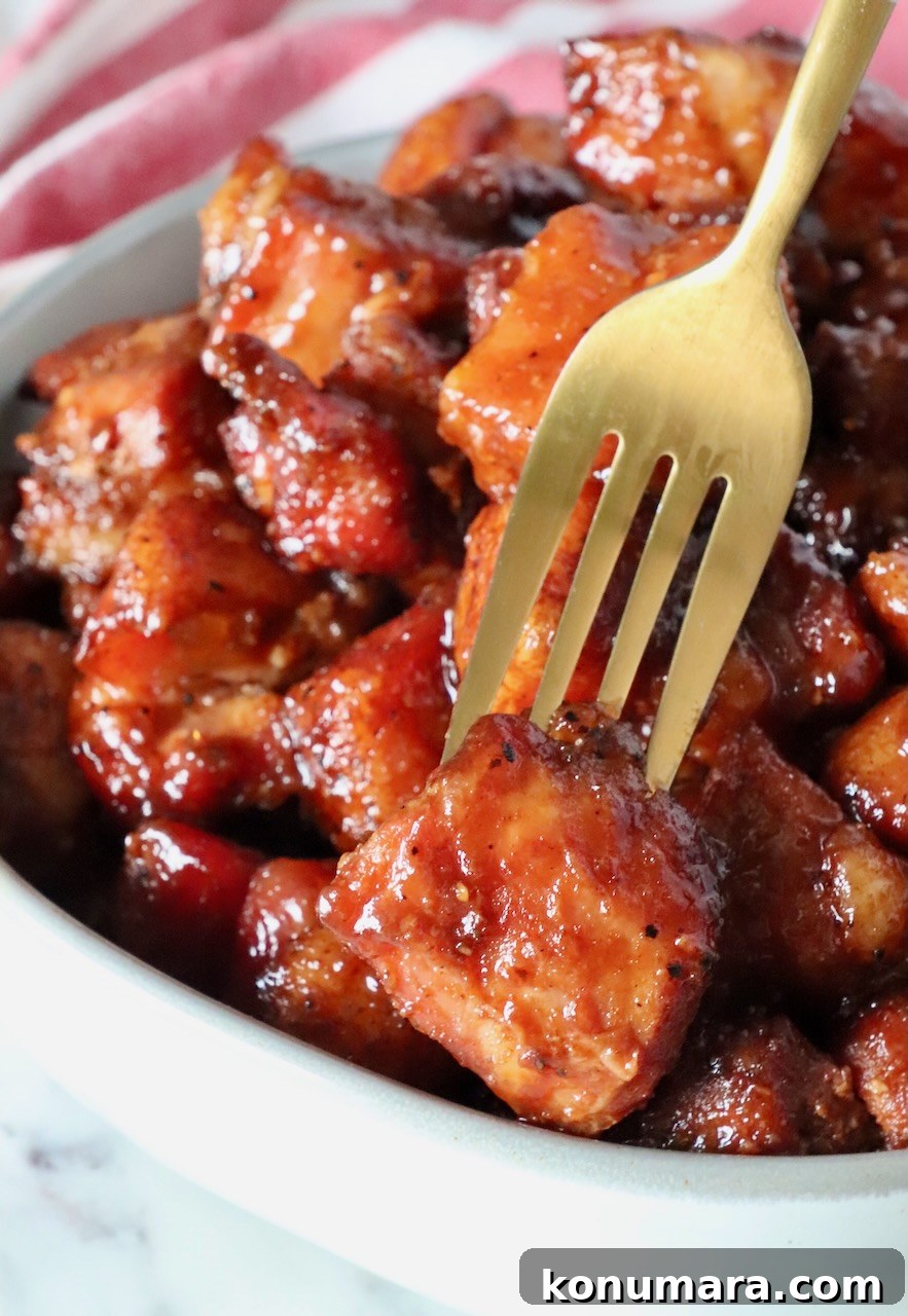 glazed cubes of smoked pork belly in a bowl with a gold fork in one piece of the pork belly
