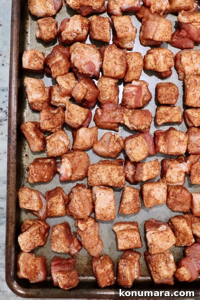 seasoned cubes of raw pork belly on a metal baking sheet
