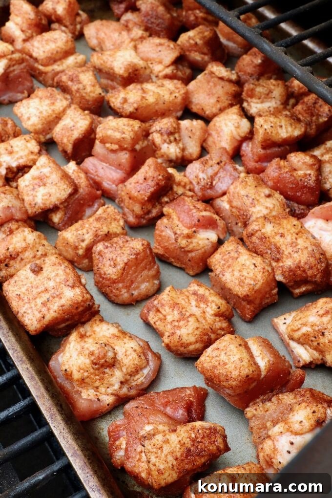 seasoned cubes of pork belly on a metal baking sheet in a smoker