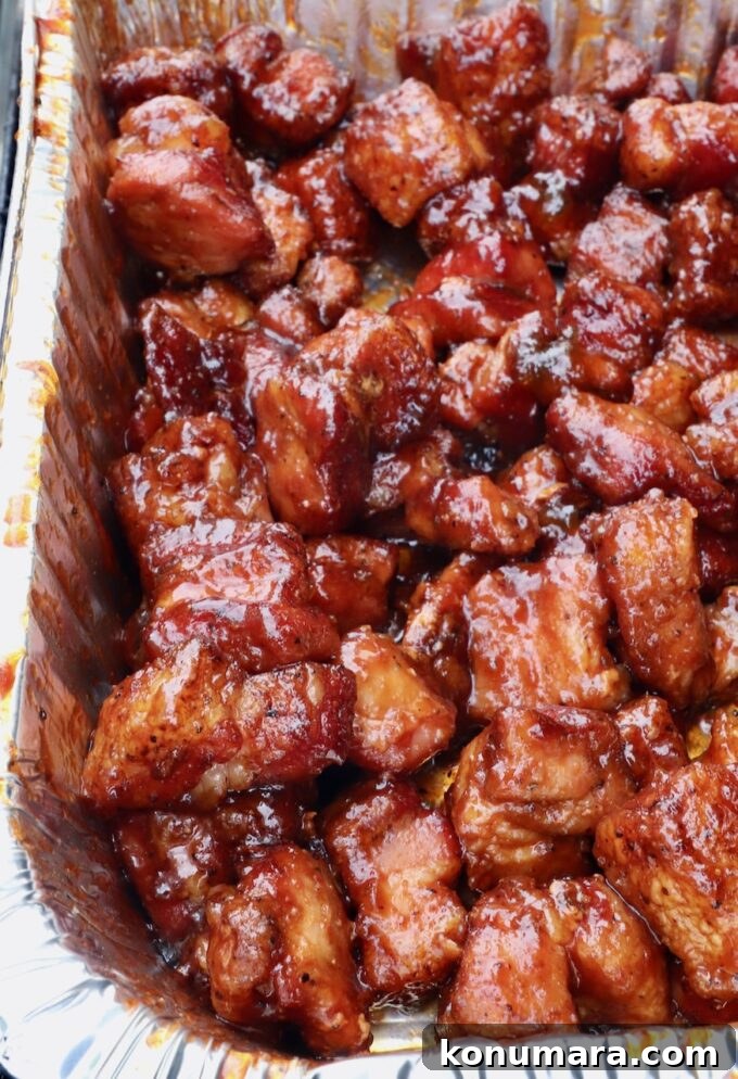 smoked cubes of pork belly in a foil pan tossed in a bbq glaze