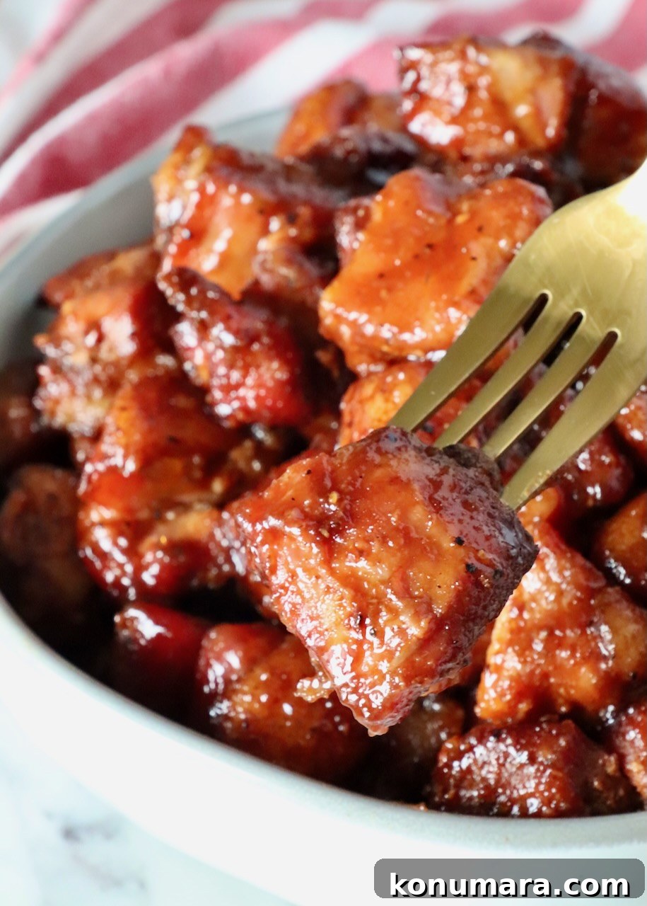 fork in a pork belly burnt end held over a bowl of smoked pork belly cubes