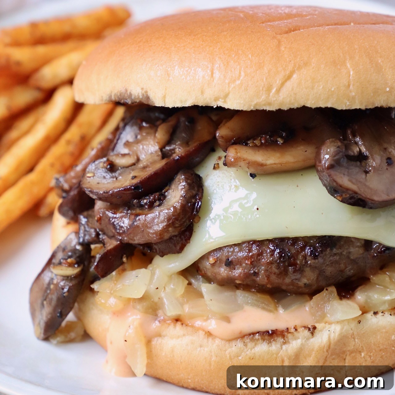 cooked cheeseburger topped with sauteed mushrooms on plate with seasoned fries