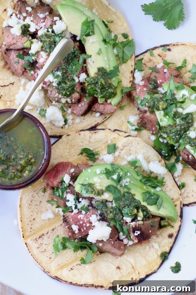 three tacos on white plate with a small bowl of chimichurri sauce on the side