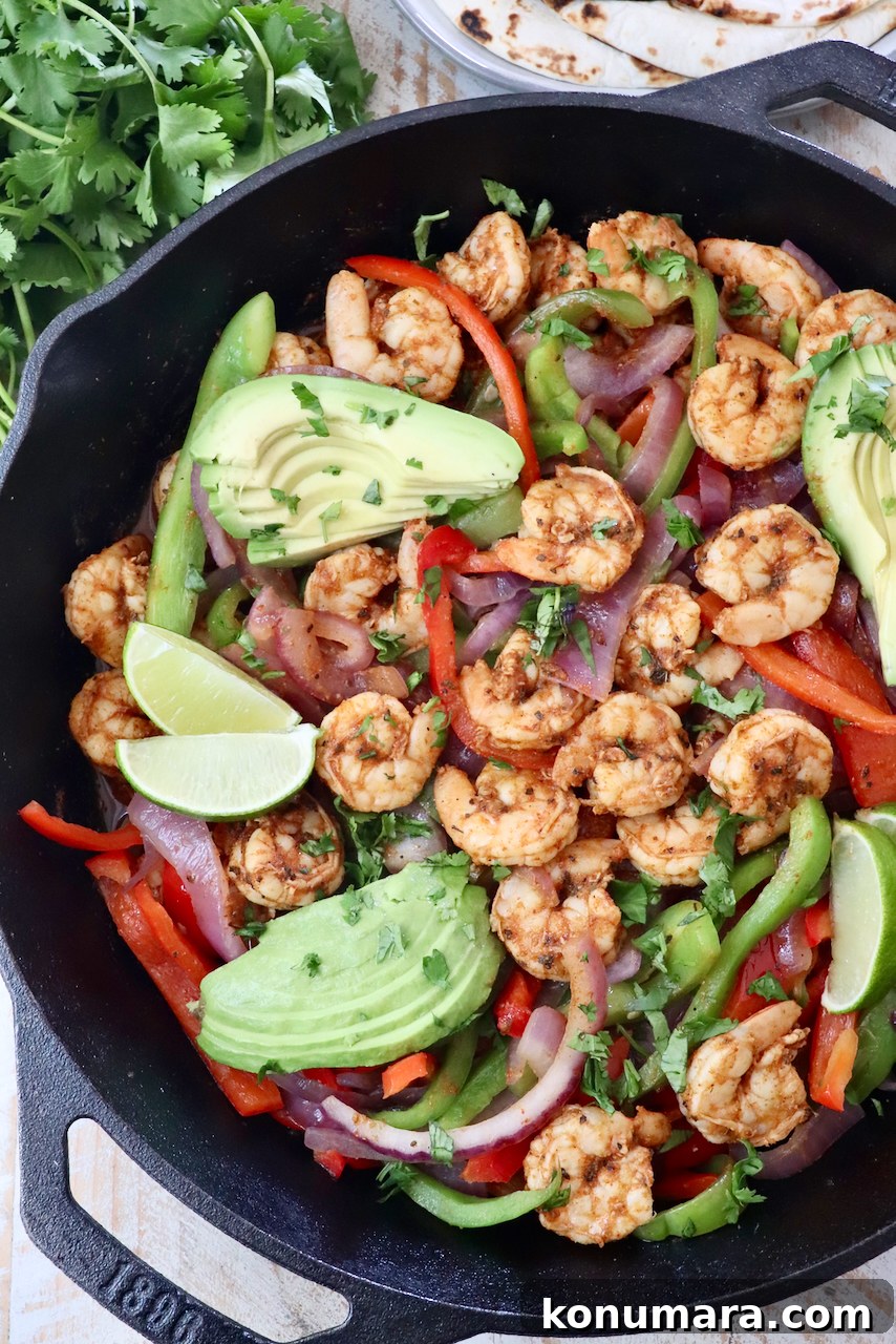 shrimp fajitas in a cast iron skillet topped with sliced avocado and lime wedges