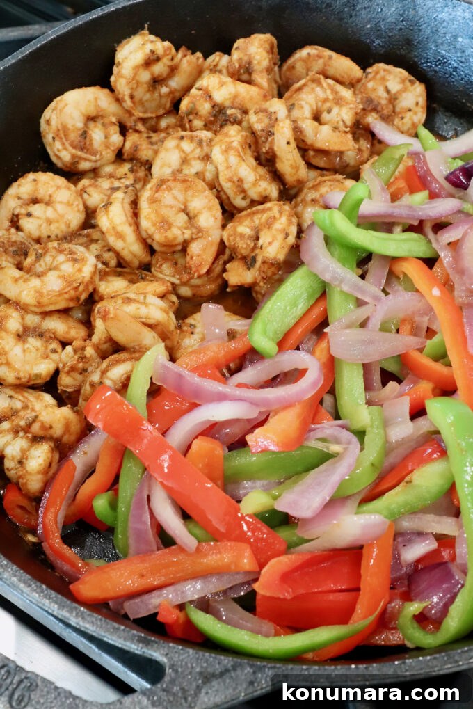 seasoned cooked shrimp in a cast iron skillet with sliced bell peppers and onions
