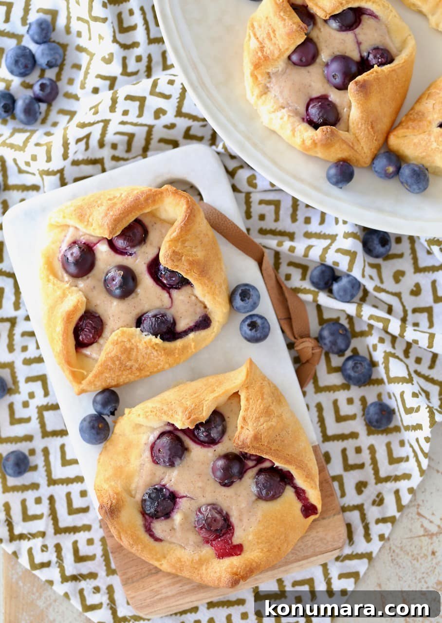 Blueberry Pastry Recipes: Flaky Treats and Baking Tips 5 Overhead shot of cream cheese blueberry pastries on cutting board and on round plate with fresh blueberries scattered around the plate