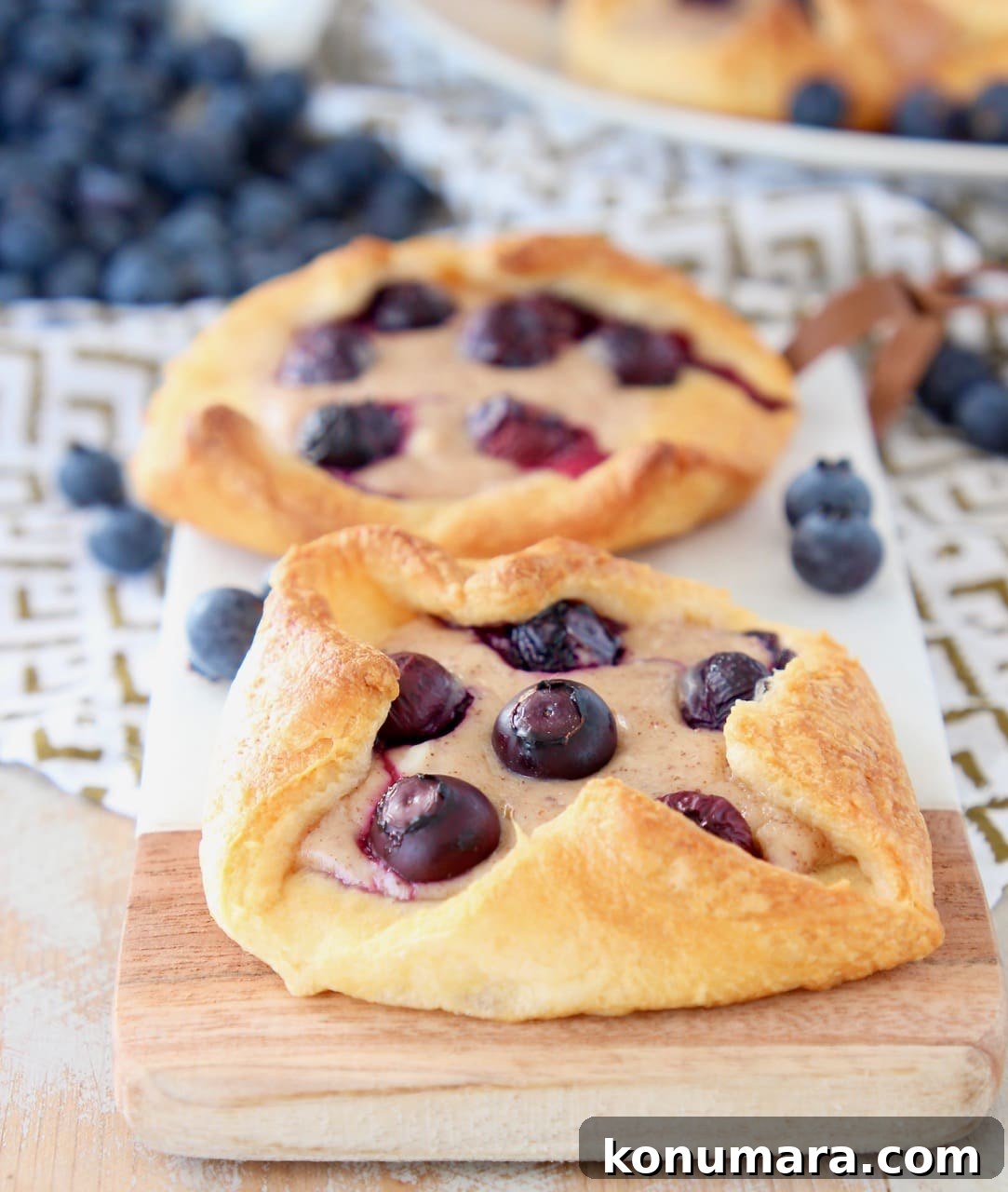 Blueberry Pastry Recipes: Flaky Treats and Baking Tips 6 Two blueberry pastries sitting on a wood and marble cutting board with fresh blueberries around and behind them