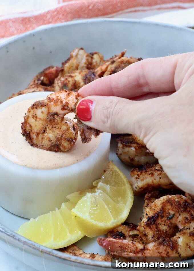 hand dipping a cooked shrimp into a bowl of creamy sauce