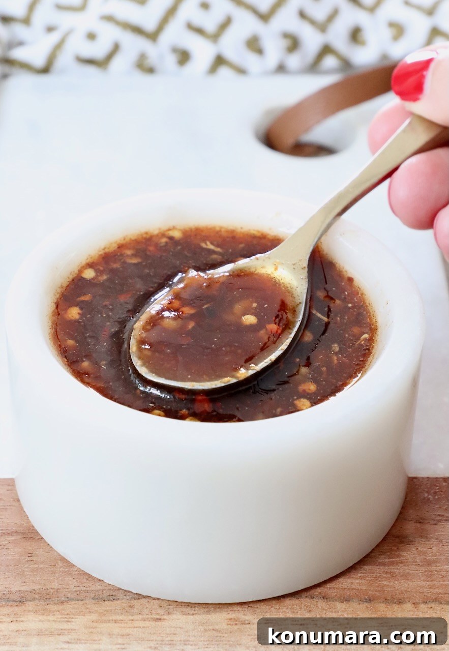 hand holding a spoon dipped into a bowl of sauce
