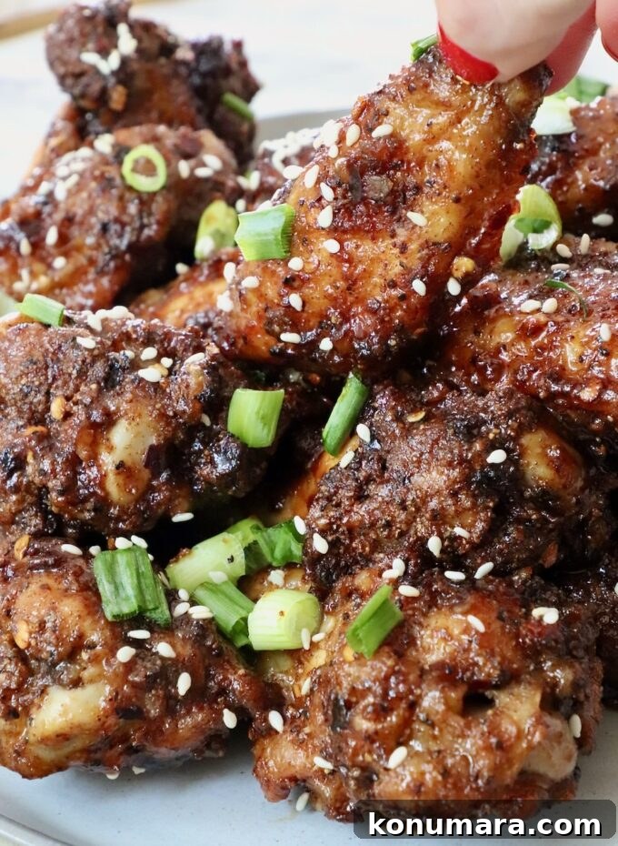 hand grabbing a chicken wing tossed in sauce piled up on other cooked chicken wings on a plate