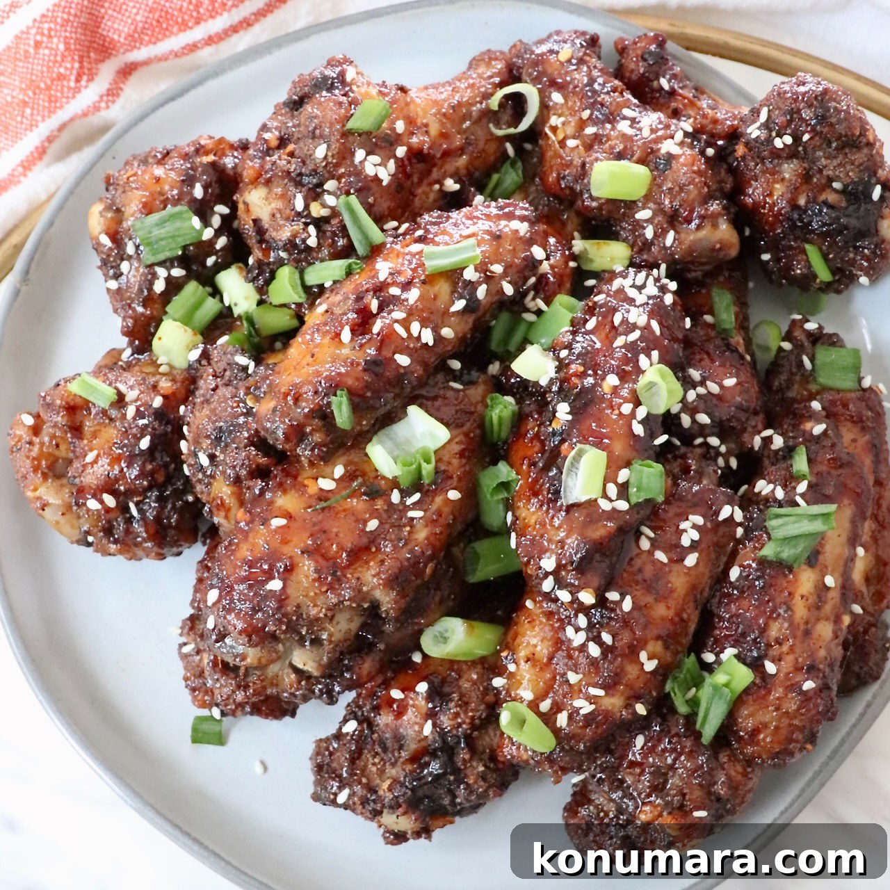 cooked chicken wings tossed in sauce and piled up on a plate with diced green onions and sesame seeds