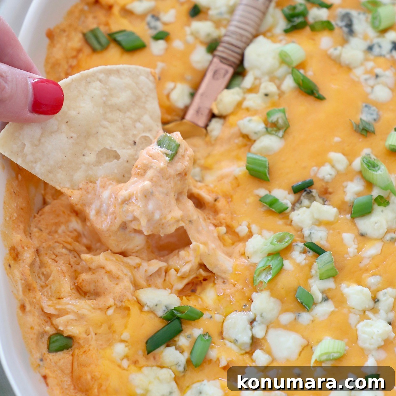 hand lifting chip out of buffalo chicken dip in baking dish