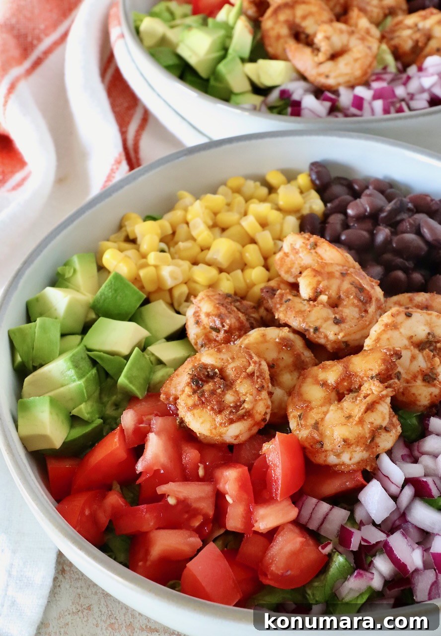 salad in a bowl with seasoned shrimp, diced avocado, red onions, black beans, corn, and tomatoes