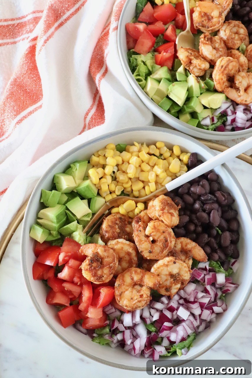 salad topped with shrimp, onion, tomato, beans, corn and avocado in a bowl with a fork