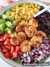 salad topped with shrimp, onion, tomato, beans, corn and avocado in a bowl with a fork