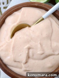 A wooden bowl filled with creamy, light orange sauce. A spoon dips into the smooth mixture.