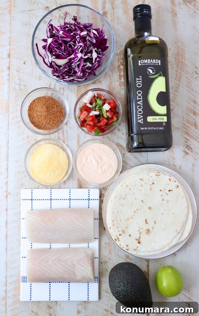 Top-down view of fish taco ingredients on a light wooden surface: red cabbage, avocado oil, taco seasoning, pico de gallo, fish taco sauce, cornmeal, tortillas, fish fillets, avocado, and a lime.