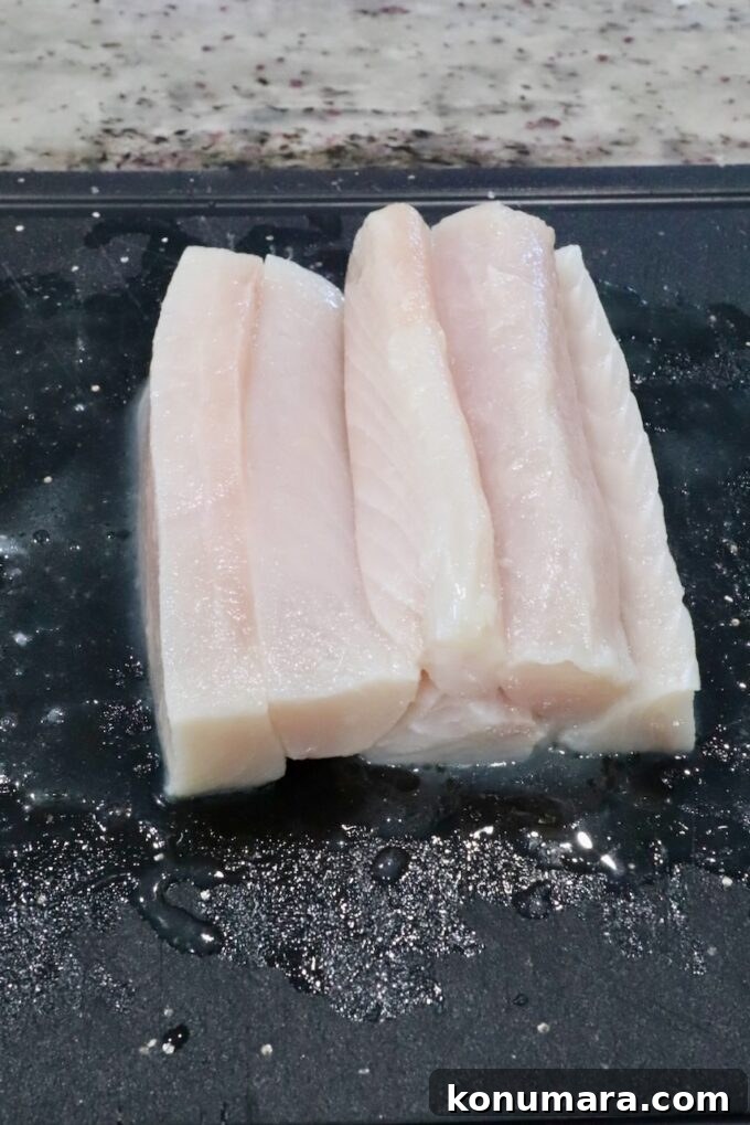 raw mahi mahi fish fillets cut into strips on a black cutting board.