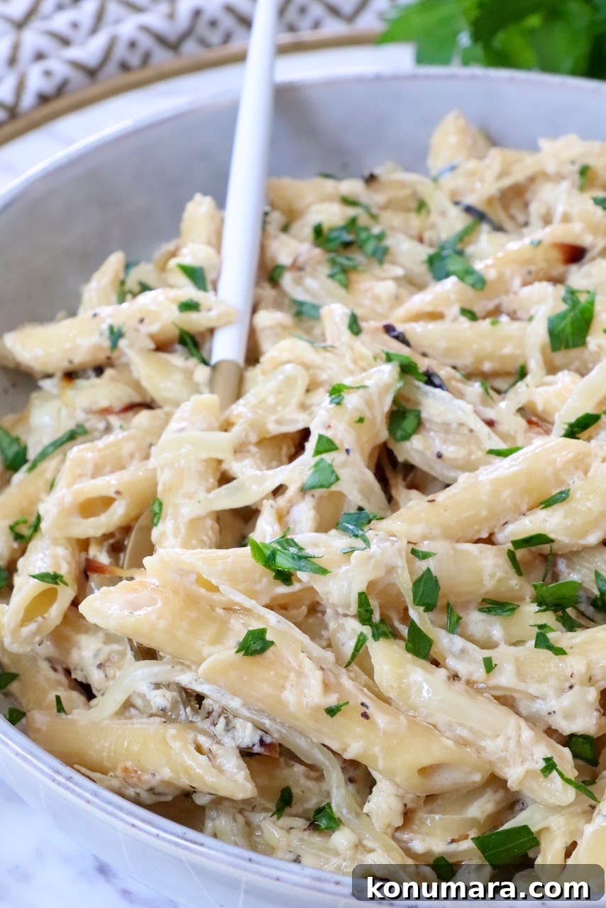 Creamy penne pasta topped with fresh parsley in a white bowl, accompanied by a white and gold spoon.