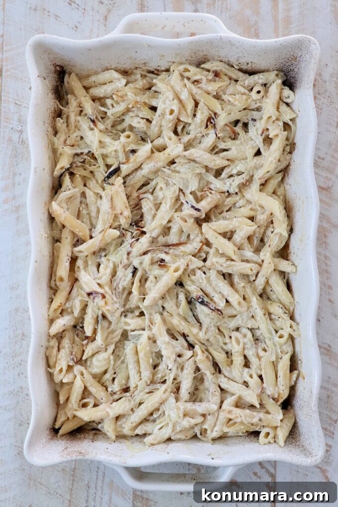Creamy baked penne pasta in a white rectangular dish on a light wooden table.