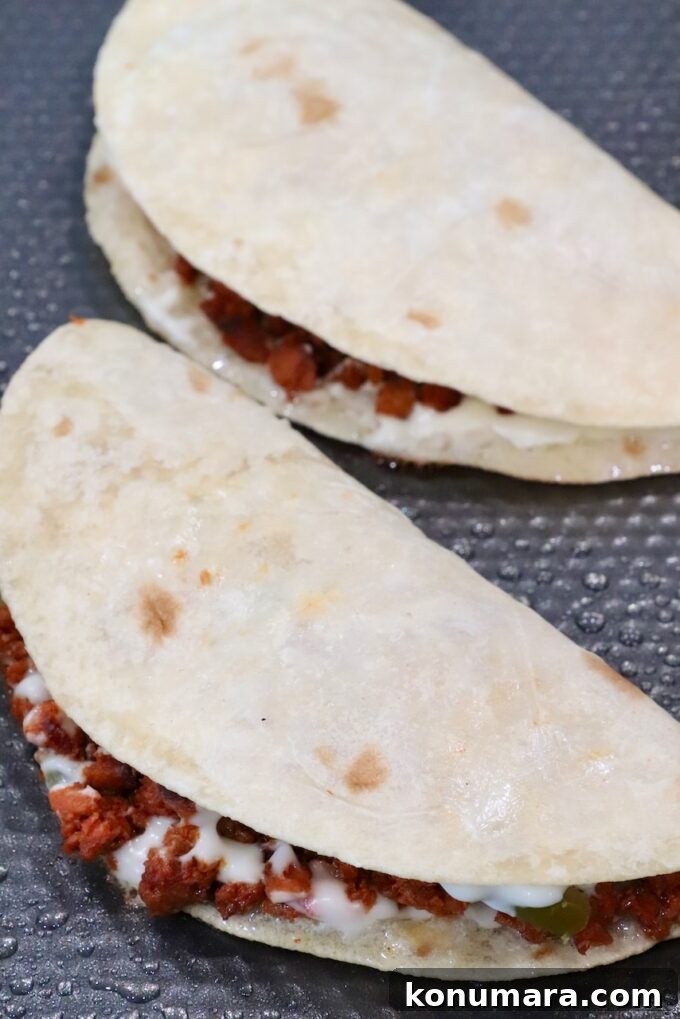 Crispy Chorizo Tacos with Melted Queso 8 Two folded soft tacos filled with chorizo and melted cheese on a textured black surface.
