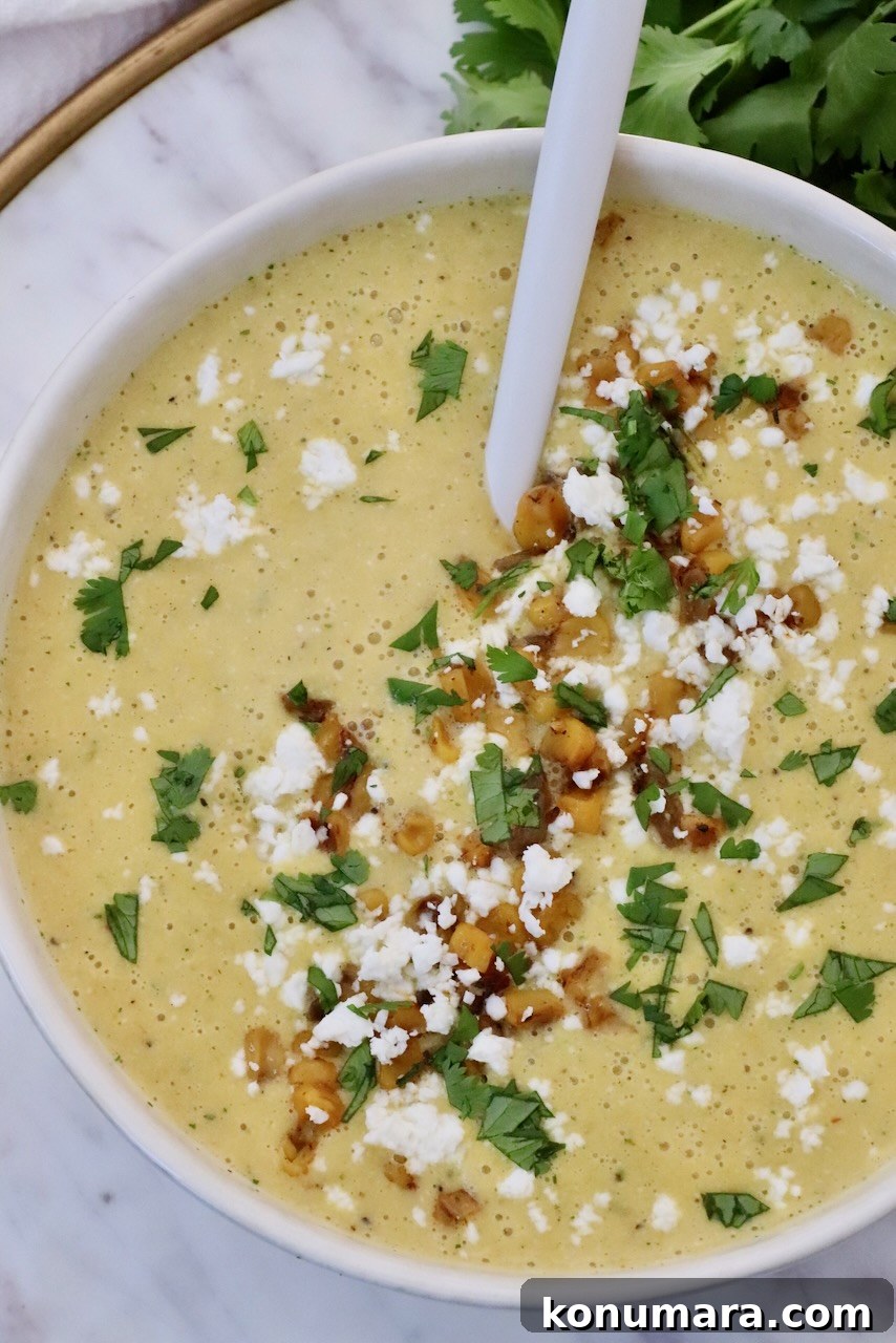 Mexican Street Corn Soup Recipe (Elote-Inspired) 2 A creamy corn soup topped with crumbled cheese, roasted corn, and chopped green herbs, served in a white bowl with a spoon.
